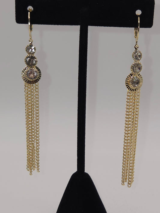 Pair of gold tassel earrings on a black stand against a gray background